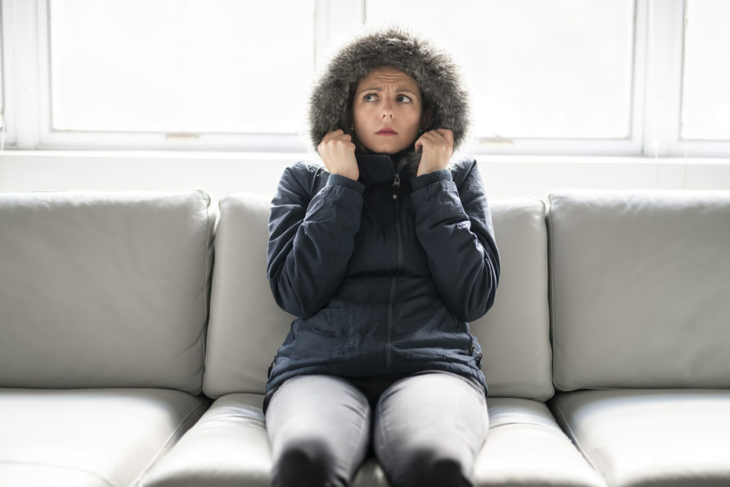 A woman on the sofa at home wearing winter coat and look concerned.