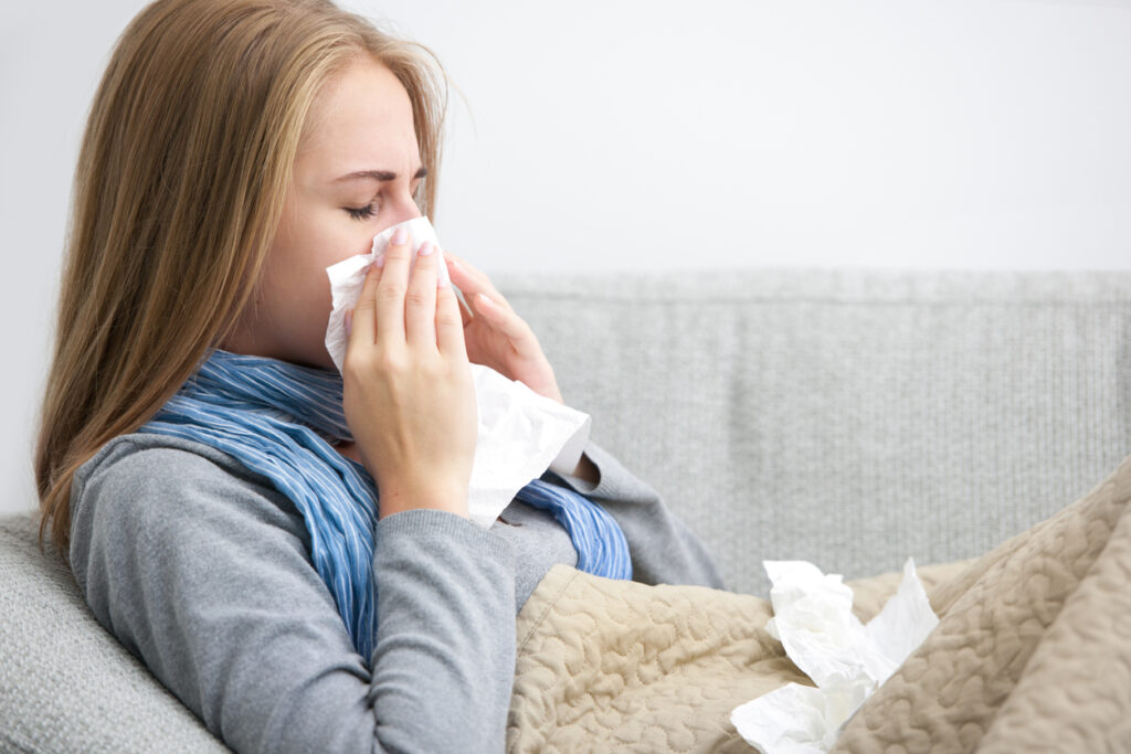 Young woman sneezing into a tissue, sitting on her couch.