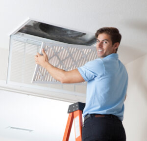 HVAC technician standing on ladder, replacing air filter and smiling.