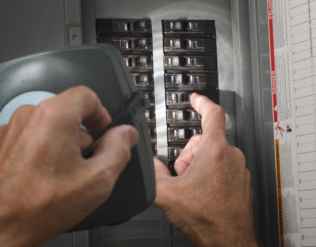 Hands holding flashlight and trying to reset an electrical panel.