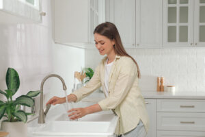 Women adding tap water to her glass from a kitchen sink.