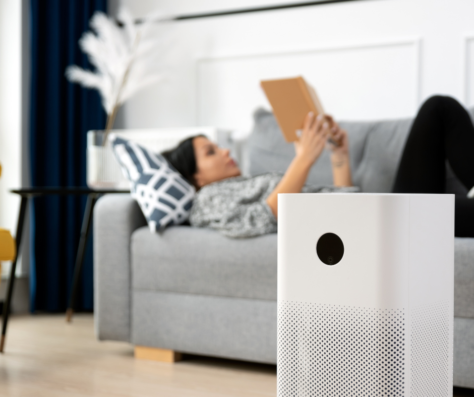 Air scrubber in living room; woman laying on couch in the background reading a book.