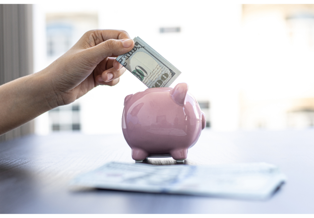 Hand putting one hundred dollar bill in pink small piggy bank.